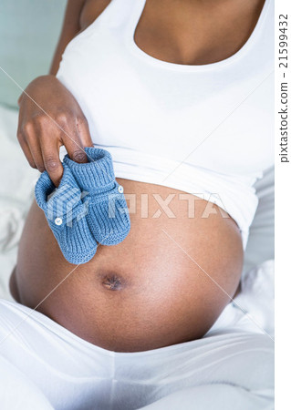 Pregnant woman holding baby shoes over bump Pregnant woman holding baby shoes over bump 21599432