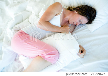 sick woman lying in bed clutching a pillow sick woman lying in bed clutching a pillow 21599674
