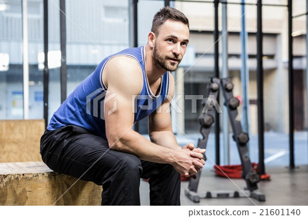 Muscular man sitting on wooden block 21601140
