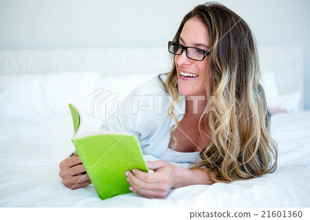 smiling woman lying on her bed reading 21601360