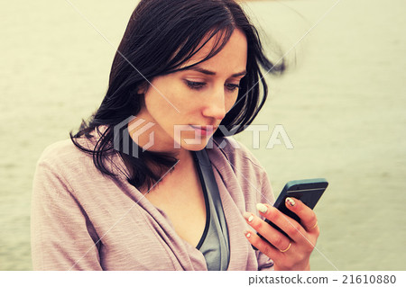 A Young Woman texting on cell phone against water 21610880