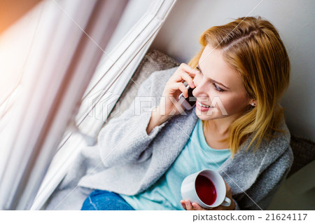 Woman on window sill with smartphone making phone 21624117