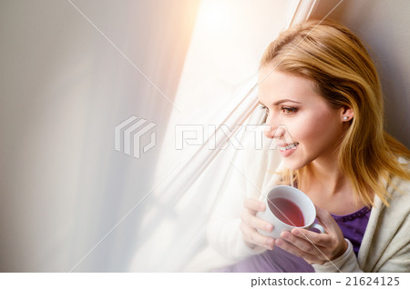 Woman on window sill holding a cup of tea Woman on window sill holding a cup of tea 21624125