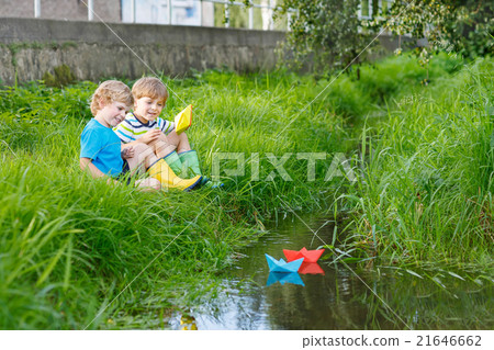 Two little brothers playing with paper boats by a Two little brothers playing with paper boats by a 21646662