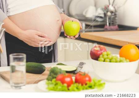 pregnant woman posing with green apple while cooki pregnant woman posing with green apple while cooki 21668223