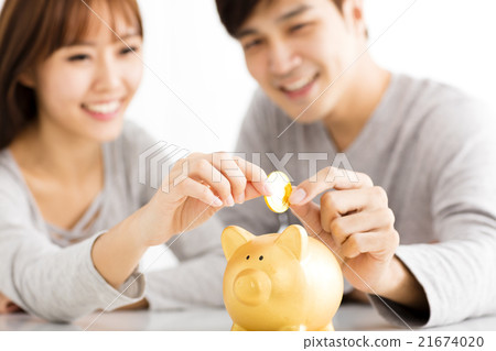 Happy young Couple Inserting Coin In Piggybank Happy young Couple Inserting Coin In Piggybank 21674020