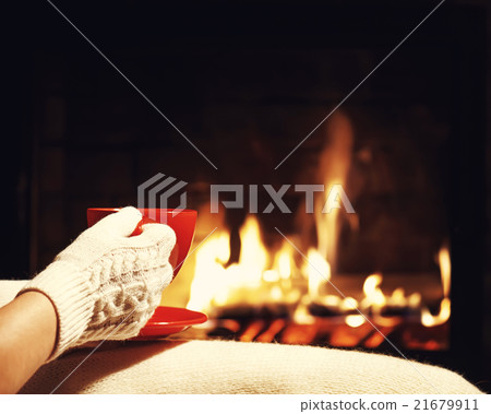 .Red cup of tea or coffee in hands near fireplace. 21679911