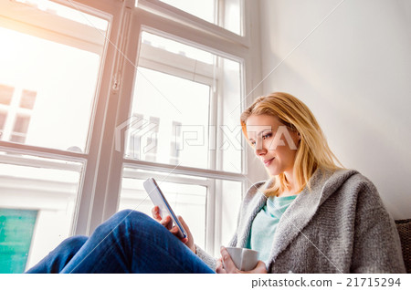 Woman sitting on window sill with smartphone and 21715294
