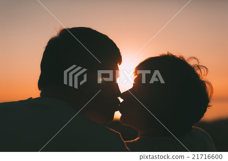 Adult married couple kiss against a sunset. Adult married couple kiss against a sunset. 21716600