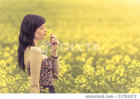 Woman in meadow of yellow flowers sniffing flower 21781972
