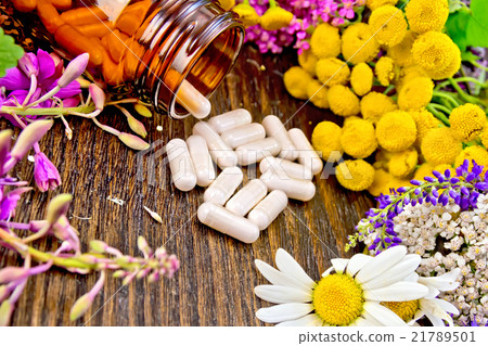 Capsules in brown jar with flowers on dark board 21789501