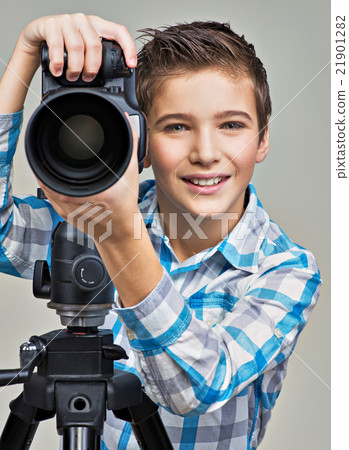 Boy with photo camera on thripod posing at studio 21901282