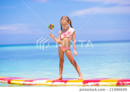 Little girl with lollipop have fun on surfboard in 21996699