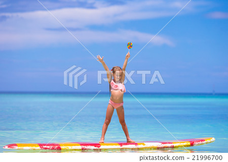 Little girl with lollipop have fun on surfboard in Little girl with lollipop have fun on surfboard in 21996700
