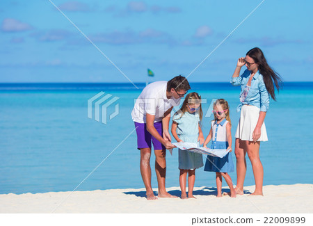Happy young family of four with map on the beach 22009899