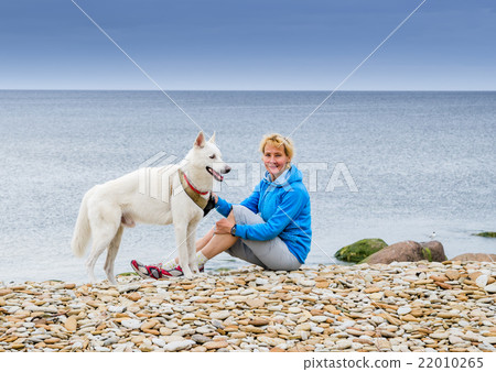 Woman  sits with a dog on the beach 22010265