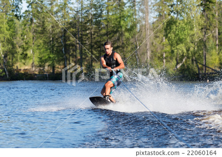 Young man riding wakeboard on summer lake 22060164