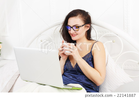 Young woman reads from tablet pc in bed, high key 22141887