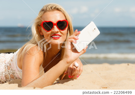 Woman lying on sandy beach using cell phone Woman lying on sandy beach using cell phone 22206499