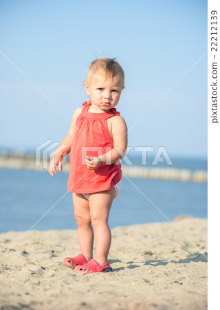 Baby girl in red dress playing on sandy beach near Baby girl in red dress playing on sandy beach near 22212139