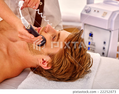 Young man receiving electric facial massage. 22252873