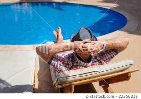 man in hat sunbathing on a sun lounger by the pool 22256812
