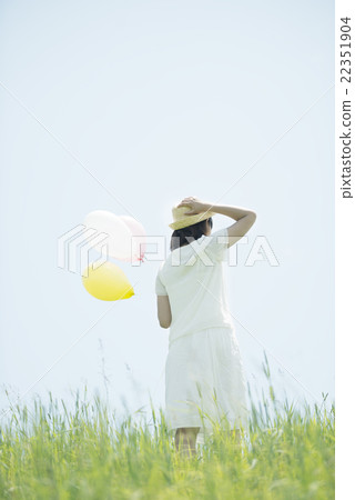 A rear view of a woman with a balloon in the meadow 22351904