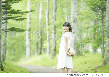 A woman holding a hat in the forest and smiling 22351998