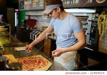 Handsome pizzaiolo making pizza at kitchen in pizzeria. Handsome pizzaiolo making pizza at kitchen in pizzeria. 22404014