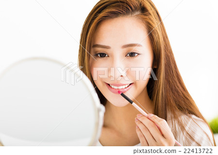 beautiful young woman putting on red lipstick beautiful young woman putting on red lipstick 22413722