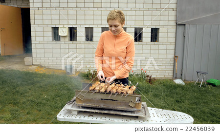 Girl cooks barbeque skewers with meat on brazier Girl cooks barbeque skewers with meat on brazier 22456039