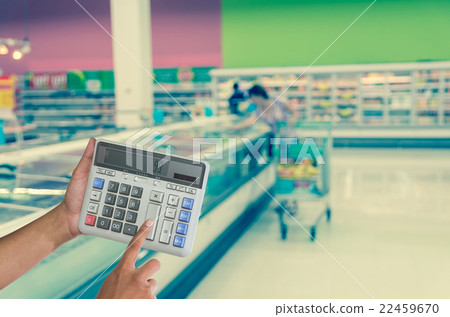 Hand touching buttons of calculator on the Abstract blurred photo of store with trolley in department store bokeh background 22459670