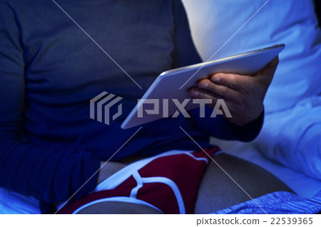 man grabbing his crotch while watches his tablet 22539365