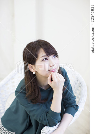 A young woman sitting in a white wisteria chair in front of a white curtain looking up A young woman sitting in a white wisteria chair in front of a white curtain looking up 22545935