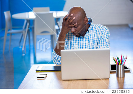 Tense man sitting on table with laptop and graphics tablet Tense man sitting on table with laptop and graphics tablet 22550825