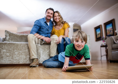 Boy using a digital tablet while parents sitting on sofa in back Boy using a digital tablet while parents sitting on sofa in back 22550826