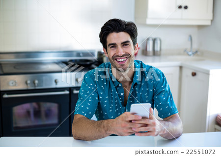 Portrait of young man using mobile phone in kitchen Portrait of young man using mobile phone in kitchen 22551072