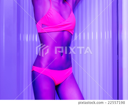 Slim young woman standing in solarium getting sun tan 22557198