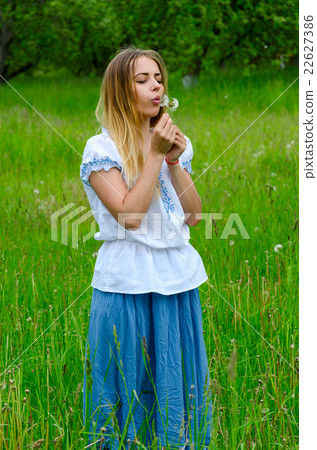 Sad young woman blowing on dandelion in hands 22627386