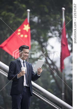Chinese businessman with a tablet computer in front of flags. Chinese businessman with a tablet computer in front of flags. 22634167