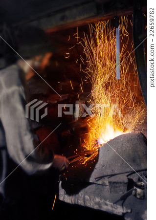 Blacksmith working near burning hearth 22659782