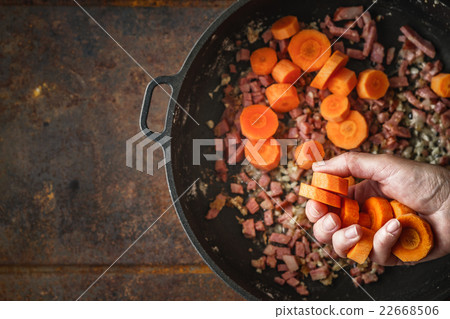 Adding carrots in the pan with bacon top view 22668506
