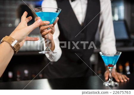 Bartender serving blue cocktail at bar counter Bartender serving blue cocktail at bar counter 22675763