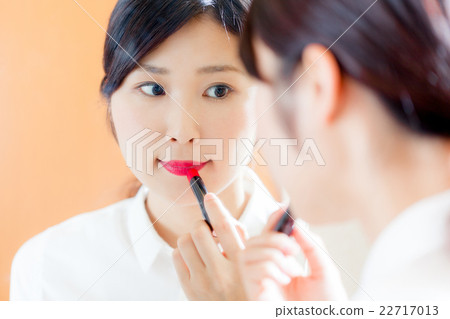 A woman applying lipstick, a mirror 22717013