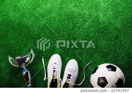 Soccer ball, cleats and trophy against green 22741567