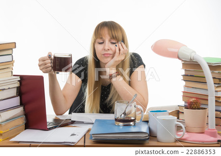 Girl student sadly and sleepily reading his thesis project sitting with a cup of coffee in hand 22886353