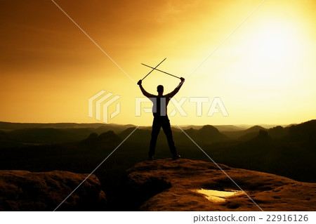 Man with crossed poles above head on rocky cliff Man with crossed poles above head on rocky cliff 22916126