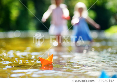 Two sisters playing with paper boats by a river Two sisters playing with paper boats by a river 22920152