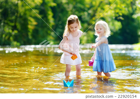 Two sisters playing with paper boats by a river 22920154