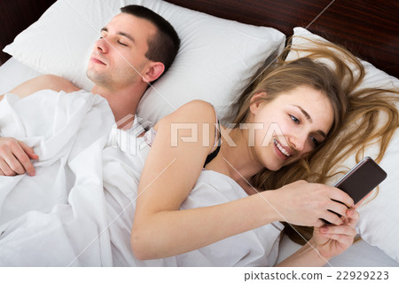 girl chatting with mobile, man sleeping by in bed girl chatting with mobile, man sleeping by in bed 22929223